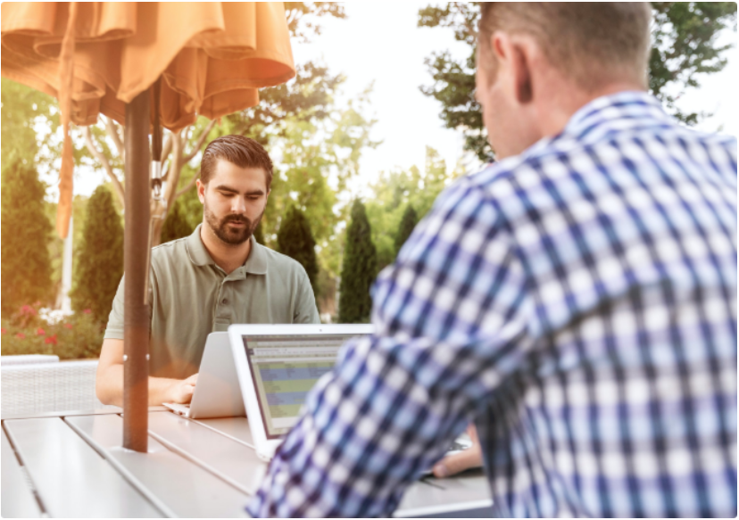 Two colleagues working on laptops at an outdoor table